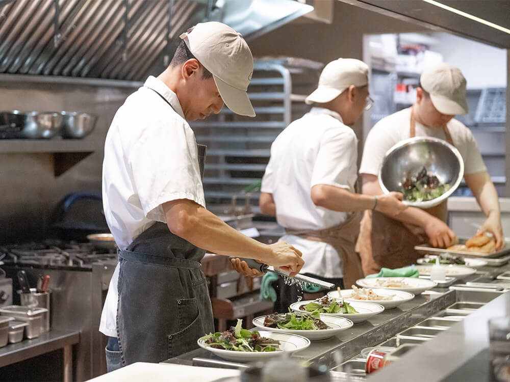 Three cooks in a kitchen plate salad for several lunches.