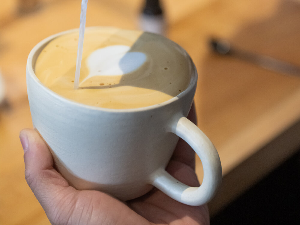 A hand holds a coffee cup while milk is poured into it, creating latte art.