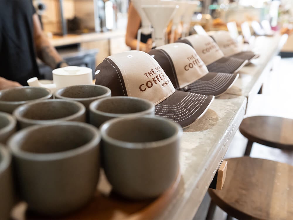 A row of cups and custom hats lined up on a counter. The hats read, “The Mazda Coffee Tour Toronto”.