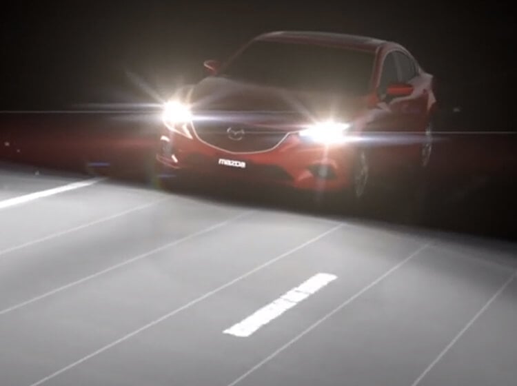 Mazda3 Sport rouge cristal vibrant sur une route sinueuse longeant une rivière vers des arbres sombres au crépuscule.