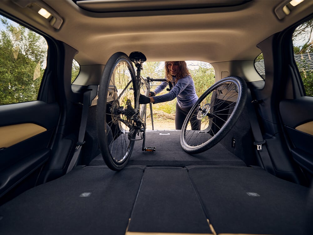 Interior view looking out the open trunk of a Mazda CX-5, with a women placing a bicycle inside.