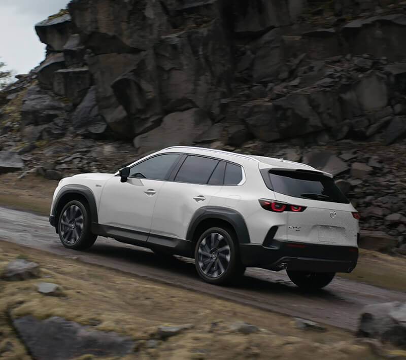 Un véhicule électrique hybride blanc monte une pente sur un terrain rocheux et montagneux. 