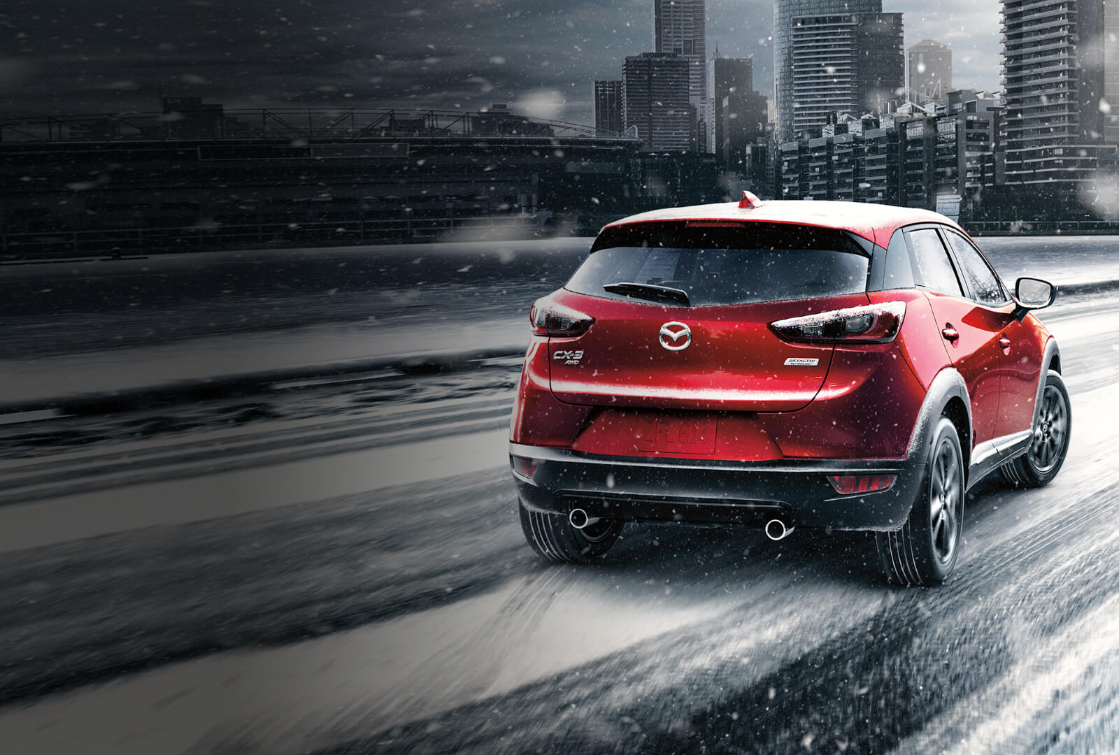 Un Mazda CX-3 rouge vibrant cristal s’engage sur une route légèrement enneigée
