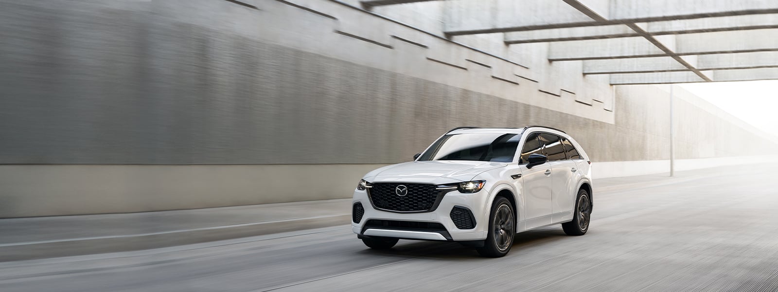 A white Mazda drives under a covered street. 