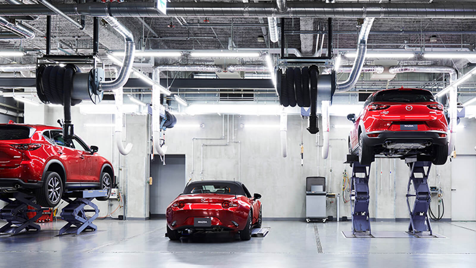 Trois Mazda rouges sont en cours de réparation dans un garage. Deux sont garées et une est surélevée. 