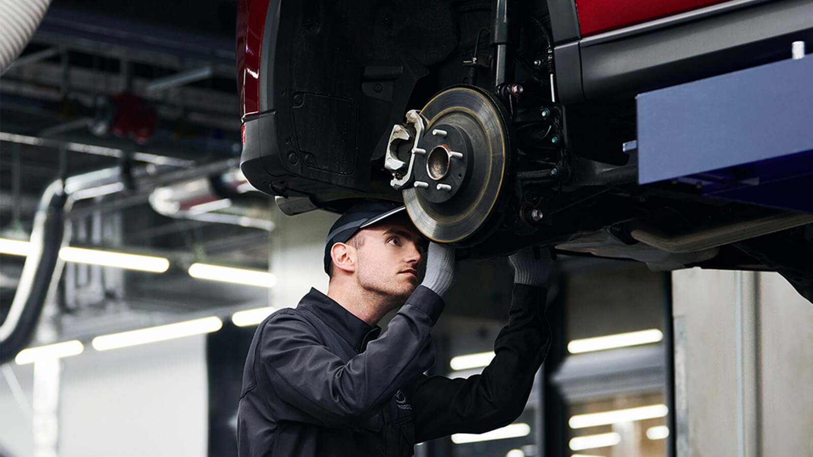 A technician works on the underside of an elevated Mazda. 