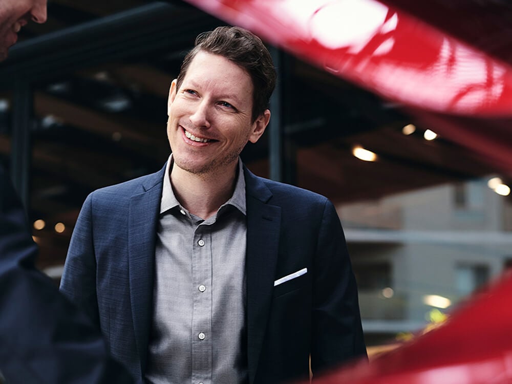 A man smiles at a technician in front of a red Mazda with its hood up. 