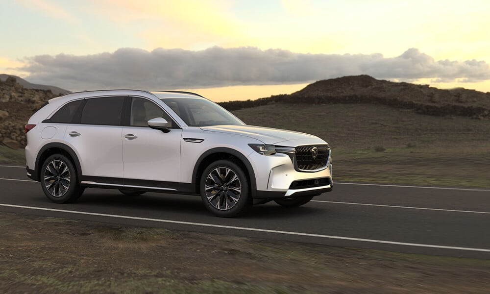 Une Mazda blanche roule sur une route longeant un terrain rocheux. 