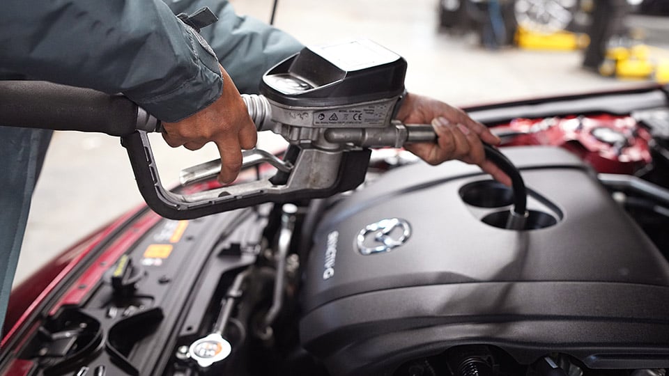 A Mazda technician putting oil into a vehicle