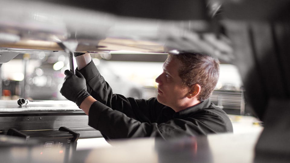 A Mazda technician working under a vehicle's engine