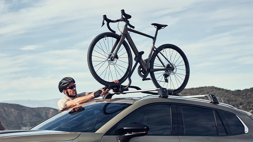 A man securing his bike to roof mounted bike carrier on a CX-50