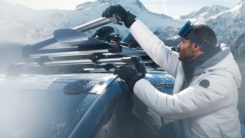 A man standing next to a Mazda3 with a roof mounted snow board carrier