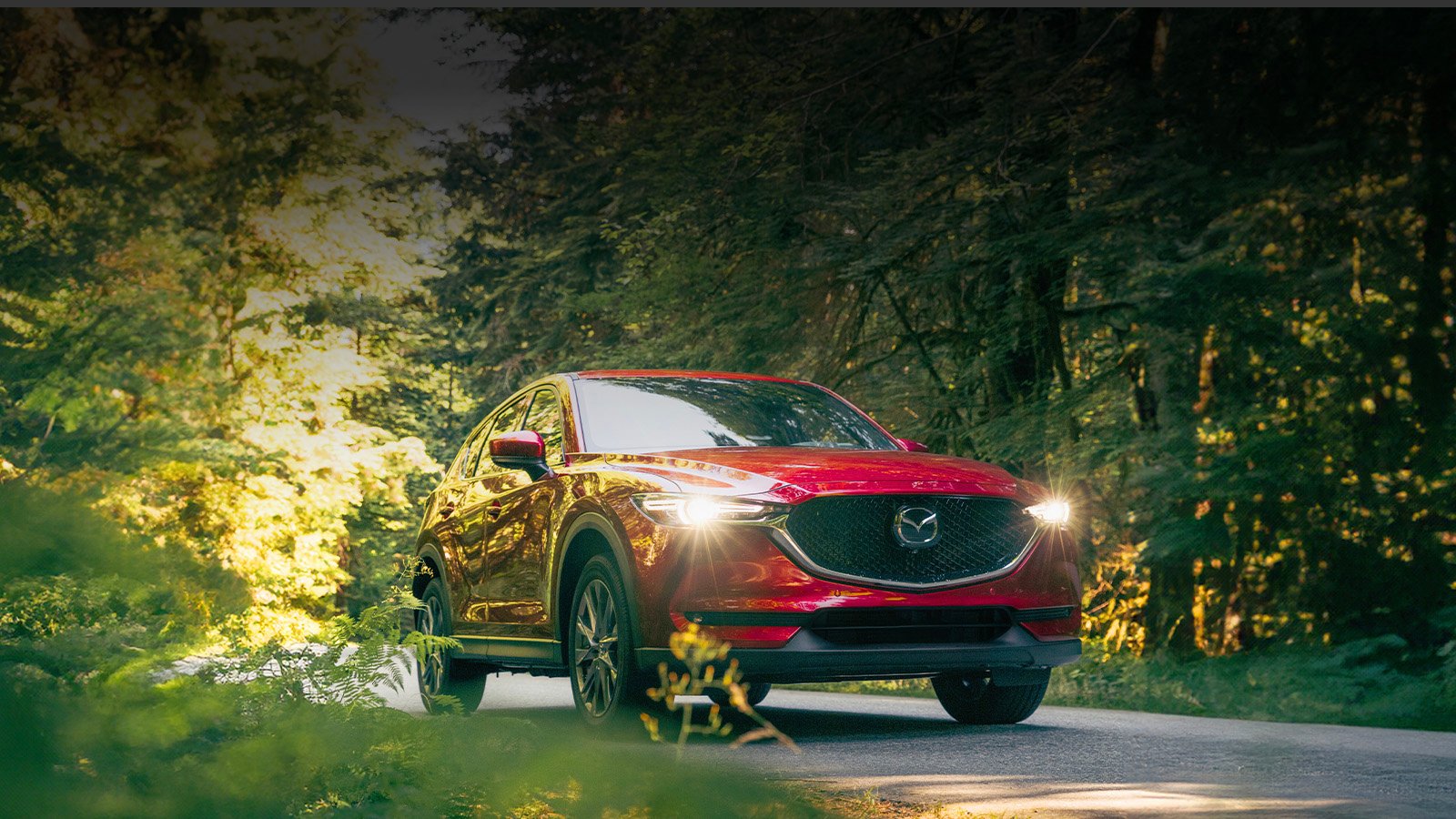 A red CX-5 driving down a road lined with trees.