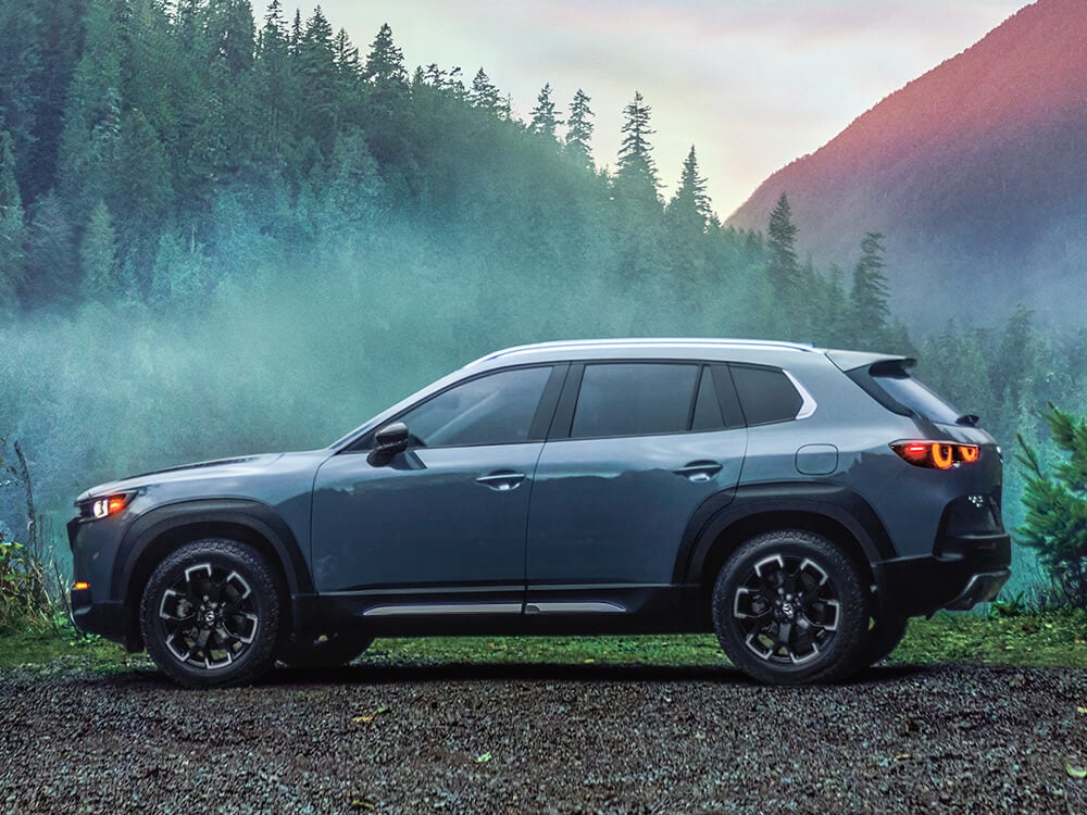 Profile shot of Meridian trim CX-50 parked atop rolling hills watching the sun set behind misty verdant mountains.  