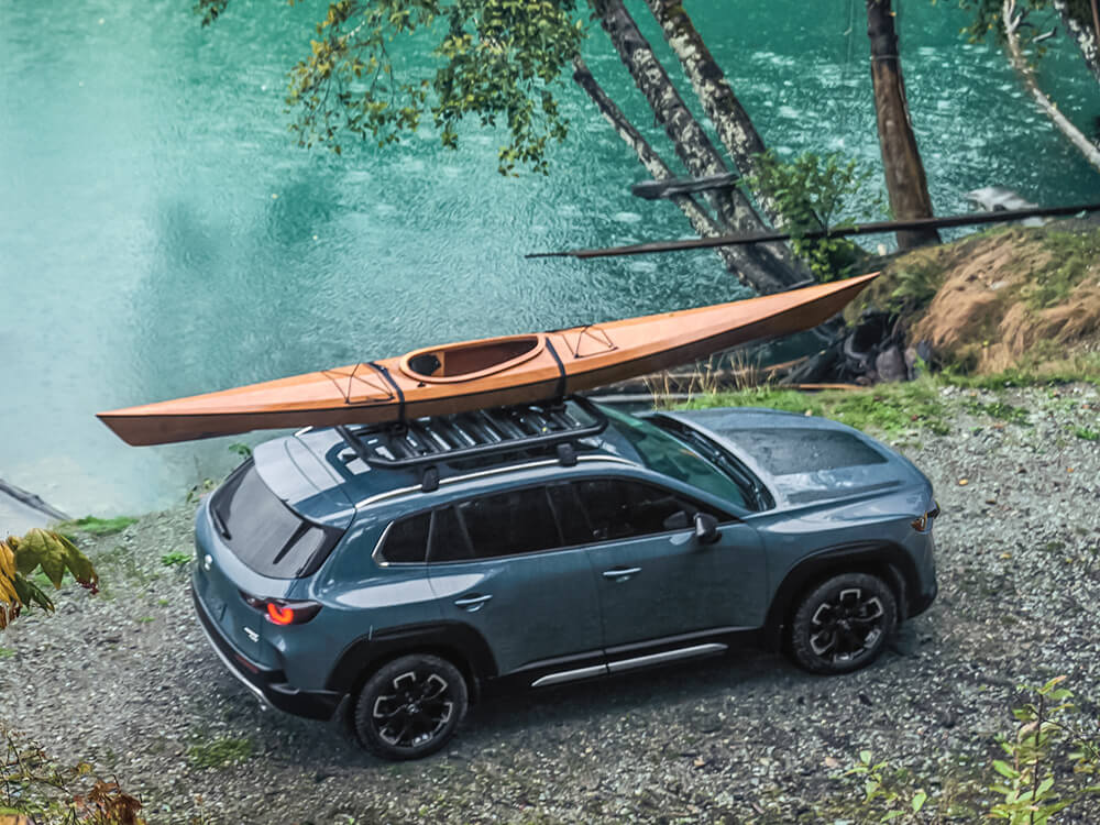 Meridian trim CX-50 parked lakeside with lights on. Kayak is loaded on roof rack. 