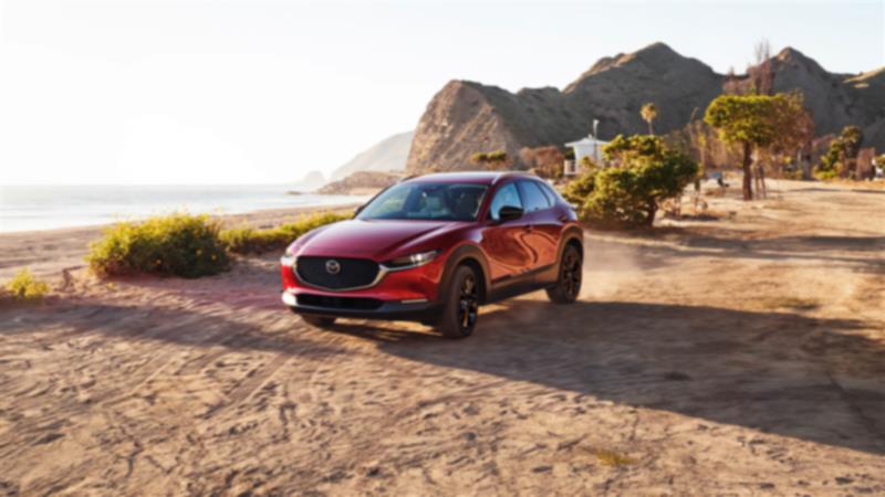 Soul Red Crystal Metallic Mazda CX-30 Crossover SUV front ¾ shot driving on gravel road beside a vast lake. 