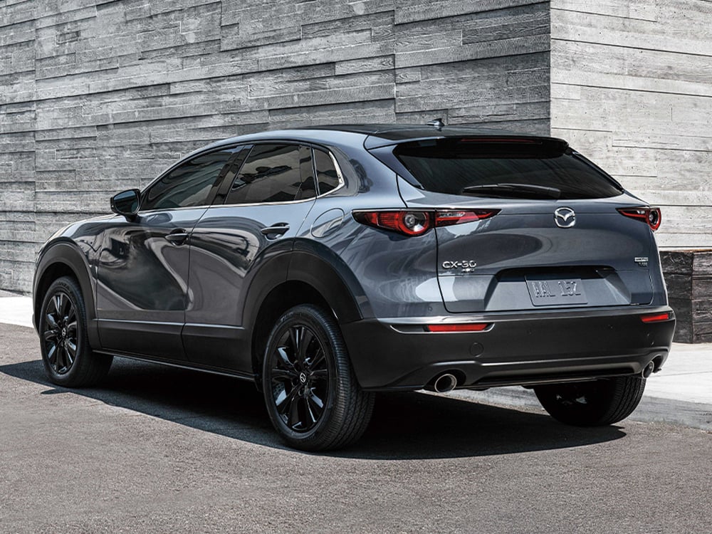 Back ¾ profile of Machine Grey Metallic Mazda CX-30 parked in front of stylish, minimal gray stone walls.