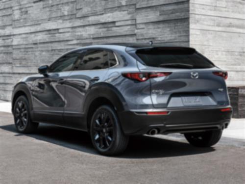 Back ¾ profile of Machine Grey Metallic Mazda CX-30 parked in front of stylish, minimal gray stone walls. 