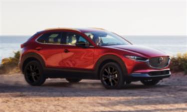 Soul Red Crystal Metallic Mazda CX-30 parked dirt road overlooking large lake in background. 