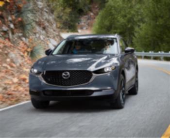 Machine Grey Metallic Mazda CX-30 takes a slight turn on an escarpment road. 