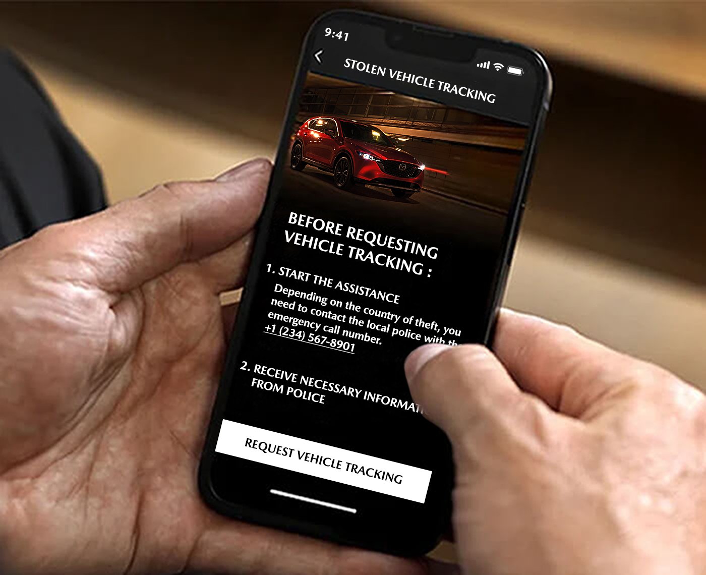 Hands holding smartphone with Mazda Stolen Vehicle Tracking on screen. 