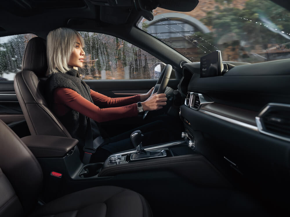 Du côté passager, vue en plongée sur une femme élégante conduisant un CX-5 avec un intérieur en cuir cacao.