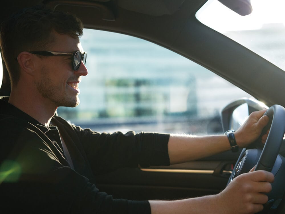 Close up view from passenger seat of smiling man wearing sunglasses driving CX-5.  