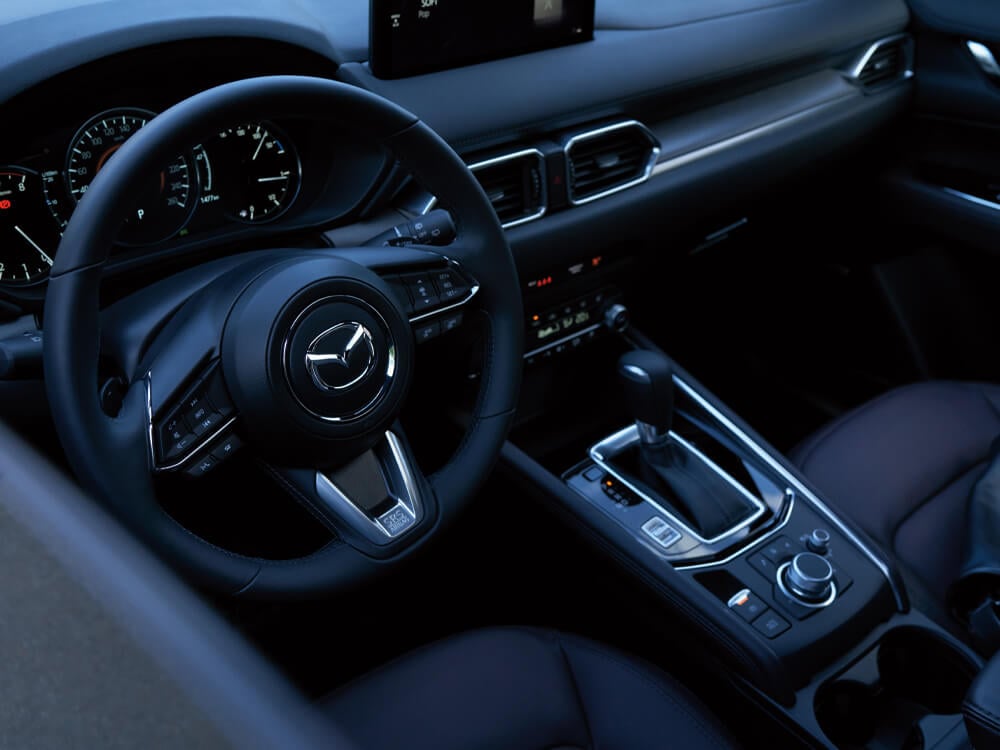 High angle looking down at CX-5 cockpit, steering wheel, console with HMI Commander switch and Cocoa leather seats.