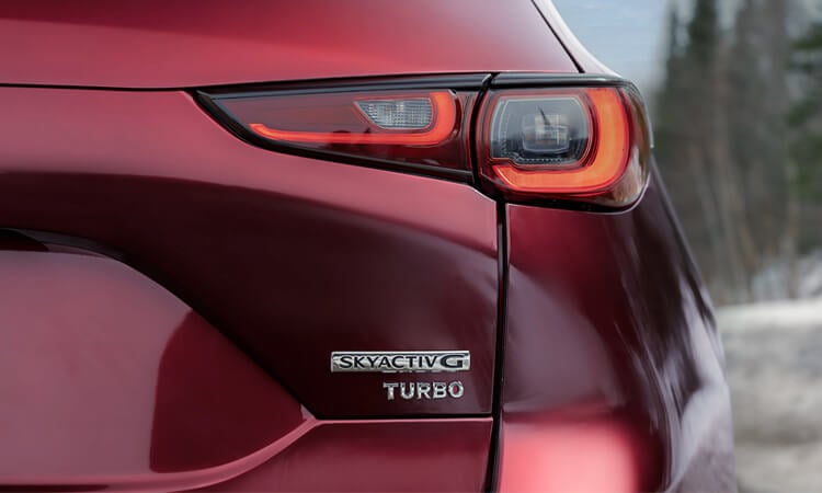 Gros plan de l’emblème Skyactiv G Turbo sur le hayon d’un Mazda CX-5 rouge vibrant cristal métallisé. 