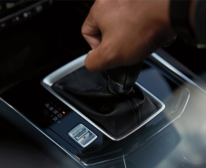 Closeup of CX-5 shifter with driver’s hand on it, and Mi-Drive mode selector switch. 