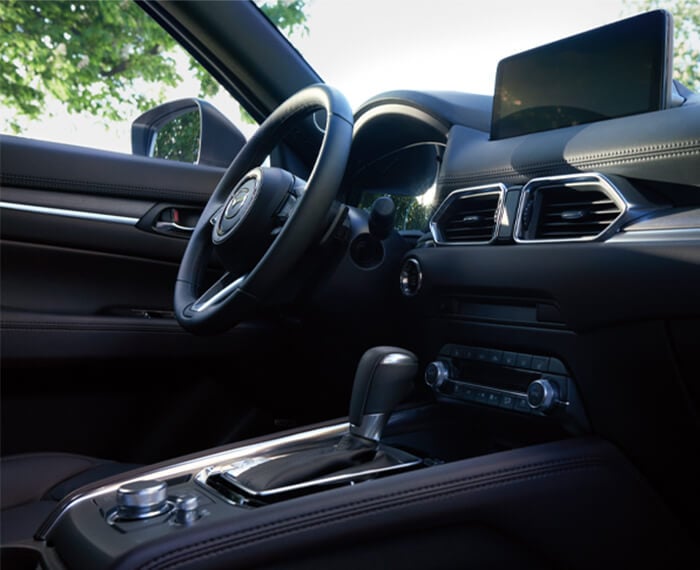 Vue en contre-plongée du volant, de la planche de bord, de l’écran et de la console d’un CX-5 depuis le siège passager. 