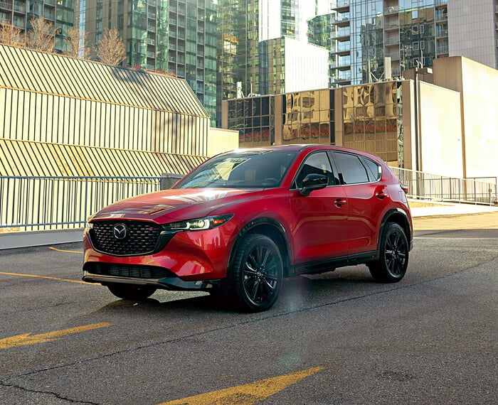 Un CX-5 rouge vibrant cristal métallisé garé au dernier étage d’un stationnement, à la lumière du jour.