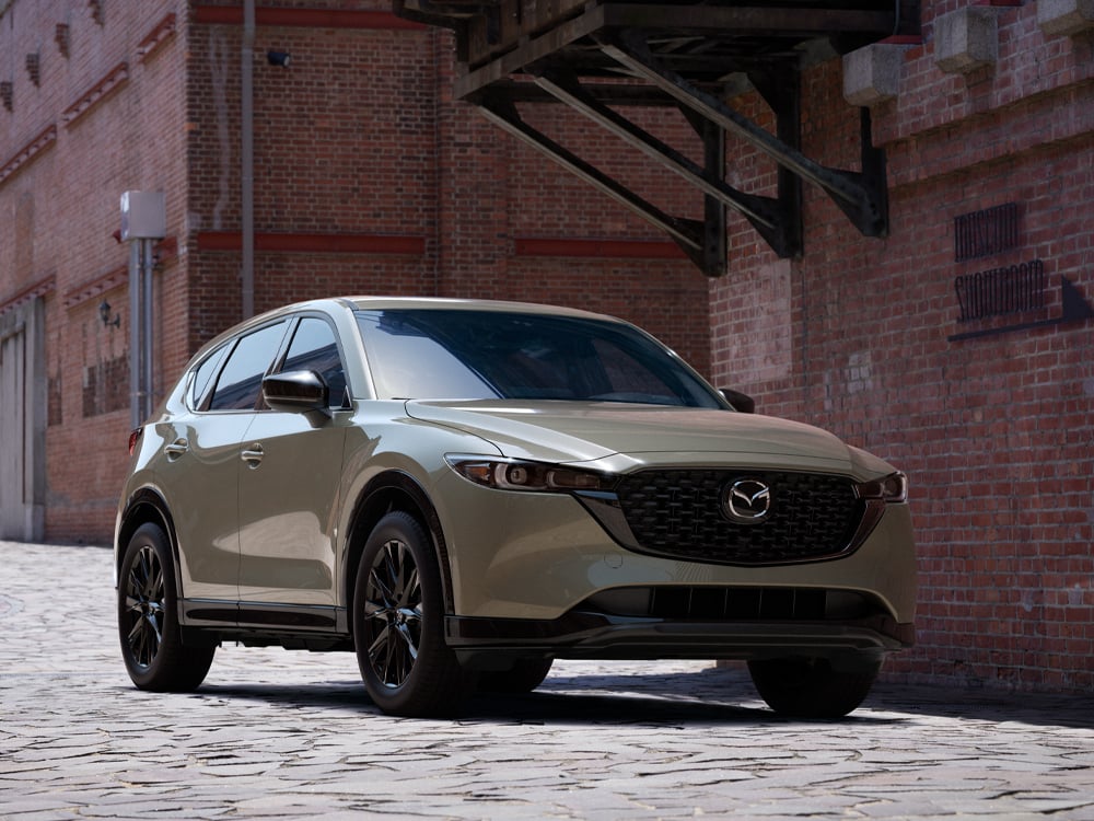 Zircon Sand Metallic CX-5 parked on cobblestone alley behind red brick buildings in day light.