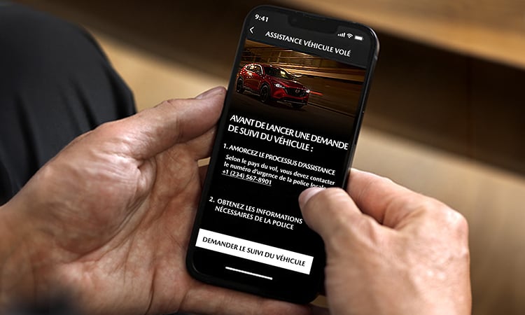 Des mains tiennent un téléphone intelligent affichant le suivi de véhicule volé de Mazda à l’écran.