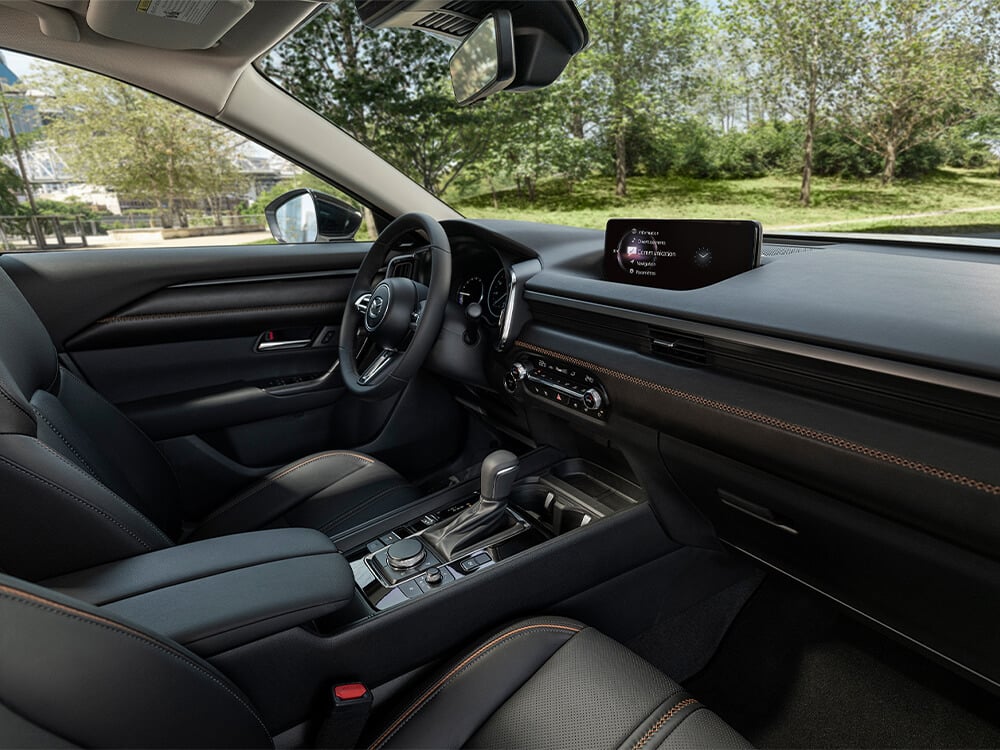 Vue du passager avant sur les sièges avant, la console, la planche de bord, le volant et les écrans d’un Mazda CX-50 hybride. 