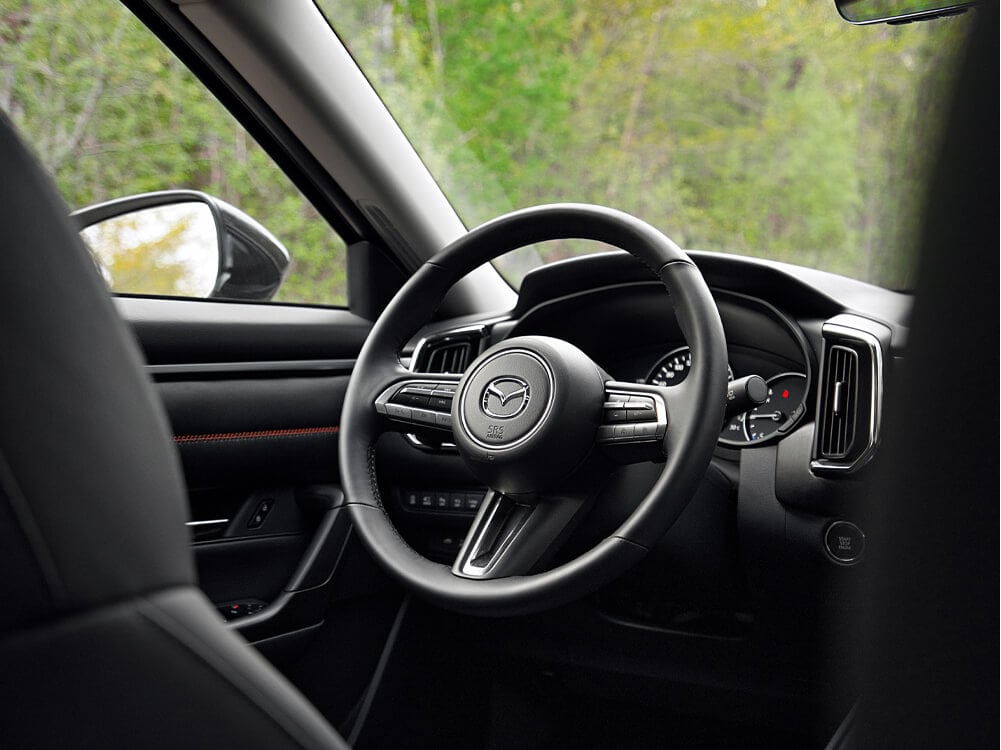 Close up of CX-50 steering wheel, dash, and front of driver’s side door. 