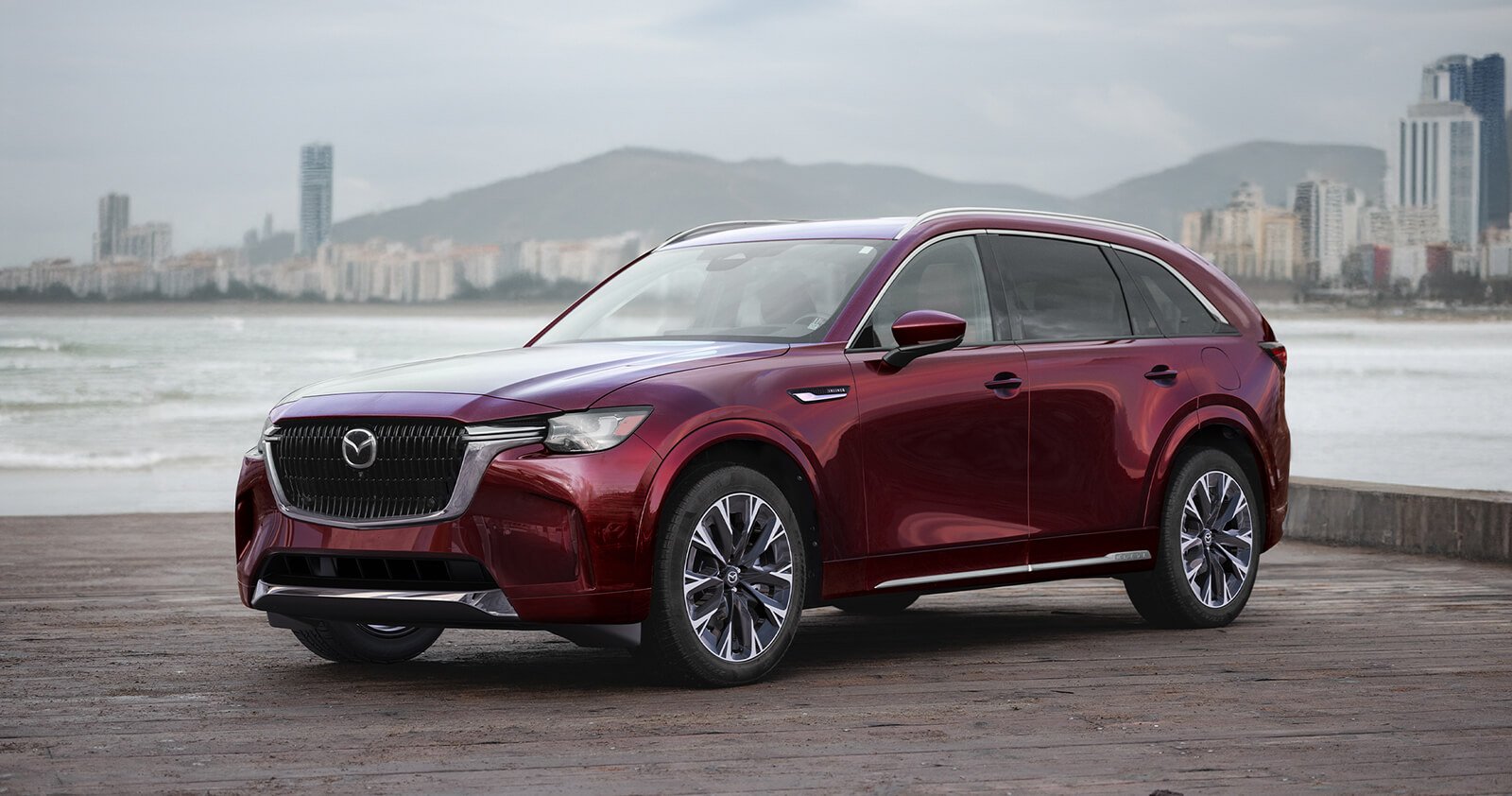 Artisan Red CX-90 parked by the water with a scenic background.