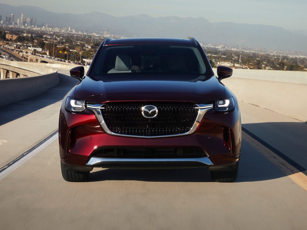 Close up of Artisan Red CX-90 driving toward camera on concrete highway overpass.