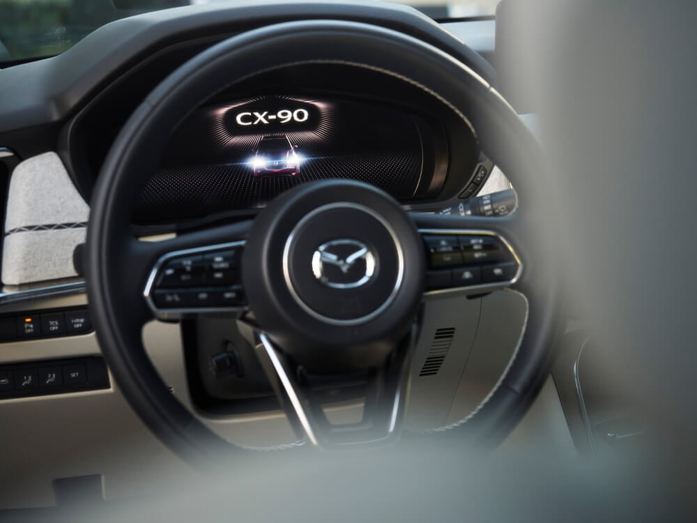 Closeup of display behind the wheel, CX-90 animates as the vehicle starts.