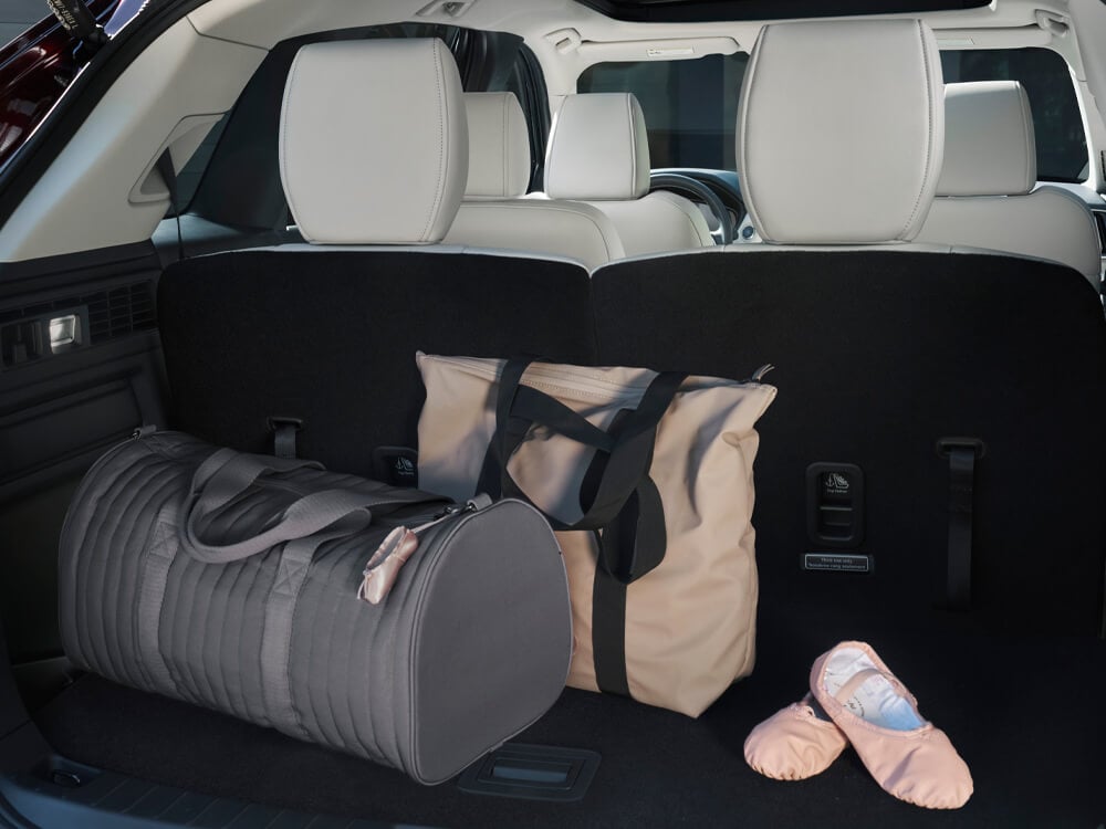 Cargo space behind 3rd row seats which are up. A duffel bag, large fabric bag, and ballet slippers are in the space.