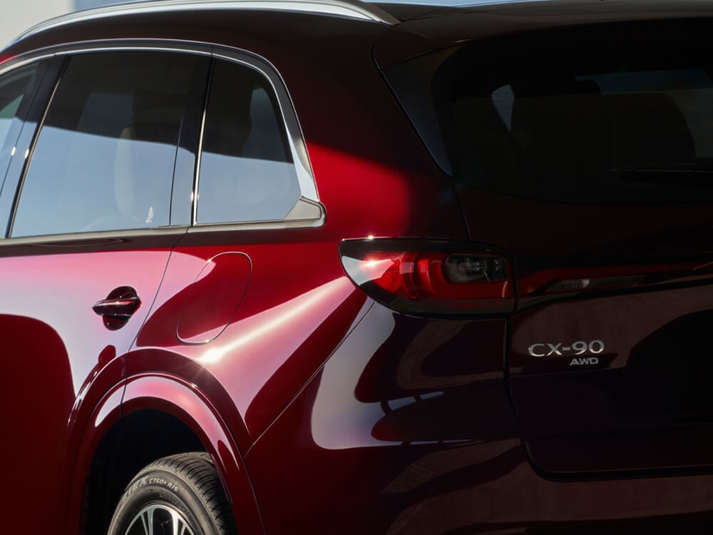 Sunlight gleaming off of the back left wheel well and taillight of an Artisan Red CX-90.