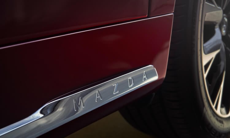 Gros plan de l’insigne Mazda sur la garniture extérieure du seuil de porte d’un CX-90 rouge artisan.