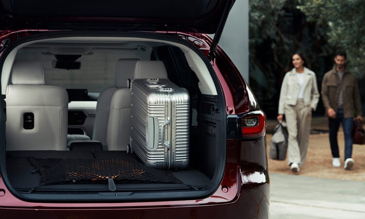 Couple approaches Artisan Red CX-90 with back lift gate open revealing a large silver suitcase.