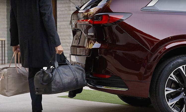 A man with hands full uses foot to activate hands-free power liftgate on Artisan Red CX-90.