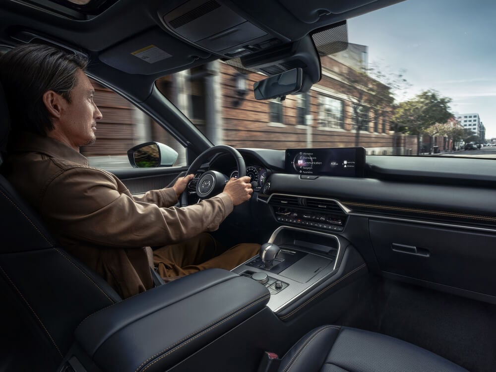 Passenger seat view of driver’s seat, dash, console as a man is driving on a stylish city street, buildings motion blurred outside windshield and window.  