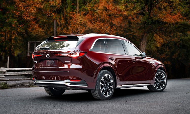 Le soleil brille sur le passage de la roue et du feu arrière gauche d’un CX-90 rouge artisan. 