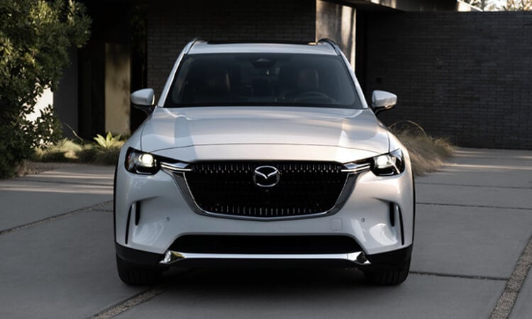 Front on shot of Arctic White CX-90 Plug-In Hybrid parked in the drive in front of a stylish home.  