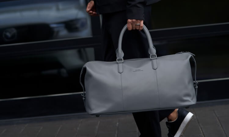 Un homme aux mains pleines utilise son pied pour activer le hayon électrique mains libres d’un CX-90 rouge artisan. 