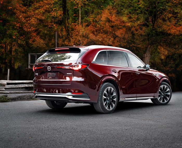 Le soleil brille sur le passage de la roue et du feu arrière gauche d’un CX-90 rouge artisan. 