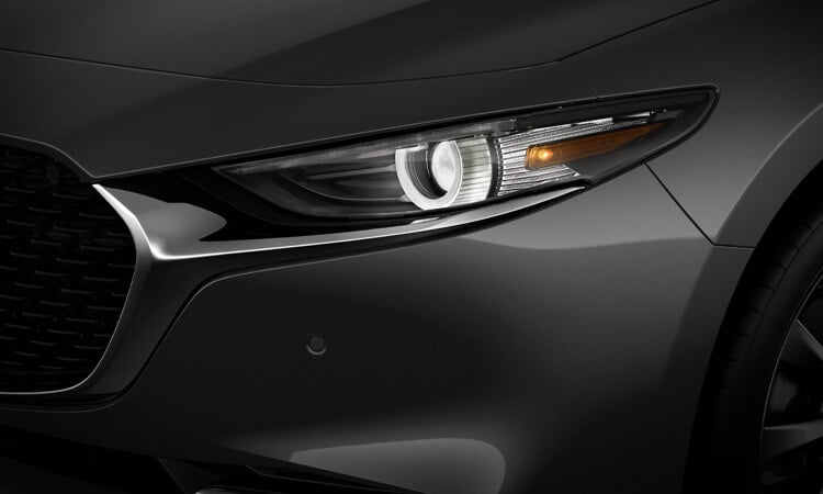 Close-up of driver’s side headlight and bumper of Machine Grey Metallic Mazda3. 